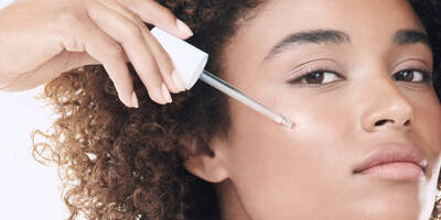 Woman with a medium skin tone applying brightening treatment serum to skin