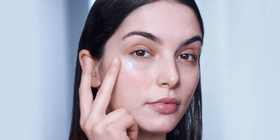 Woman showing how to apply eye cream under eyes using a tapping motion.