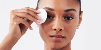 Woman with dark skin removing eye makeup with a cotton round pad and bi-facil eye makeup remover